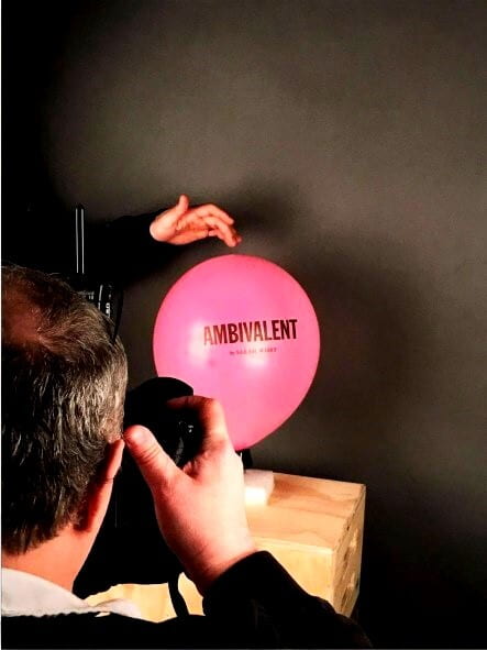 a person photographing a pink balloon with the word Ambivalent written on it.
