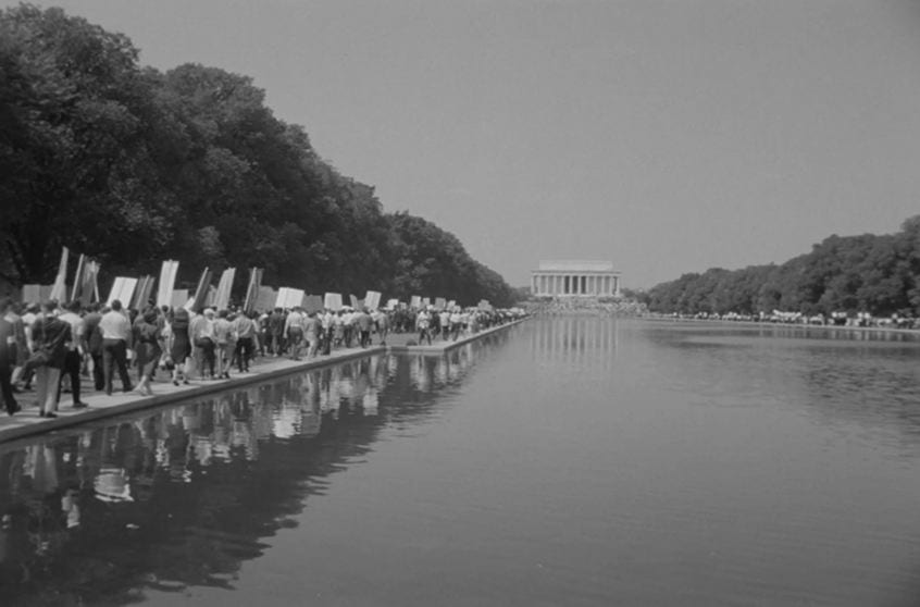 People with placards marching along the Reflecting Pool towards the Lincoln Memorial.